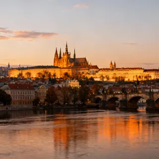 A panoramic view of Prague Castle complex from across the Vltava river, representing the ancient seat of the Bohemian Crown, bathed in golden evening light.