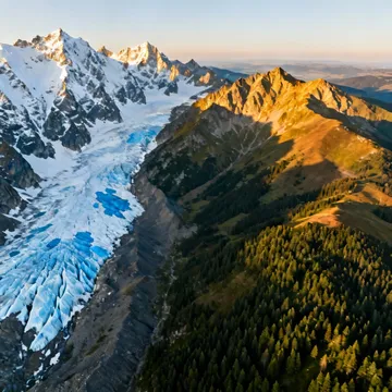 A sweeping aerial shot of a majestic Alpine range with sharp, glaciated peaks on one side and the rolling, tree-covered foothills of the Eastern European mountains (like the Krkonose) on the other, showing the stark but beautiful contrast.